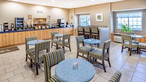 A hotel lobby with striped chairs and tables, a counter with coffee machines, and a large window. - Microtel Inn & Suites by Wyndham Johnstown (Johnstown)