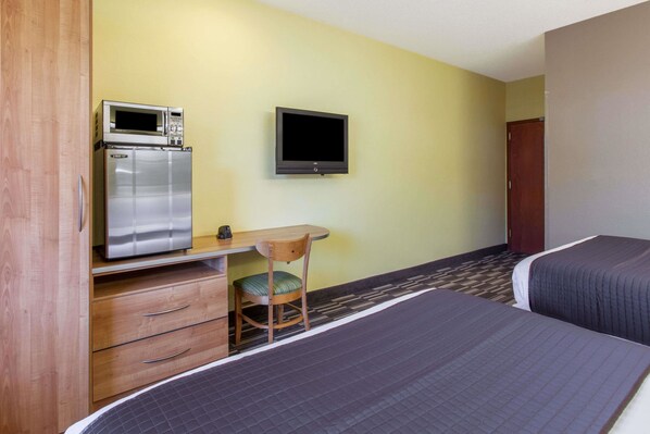 Una habitación de hotel con una cama, un escritorio con microondas, un televisor y una silla.