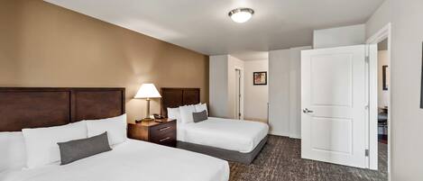 Una habitación de hotel con dos camas, una mesita de noche, una lámpara y una puerta que da a otra estancia.
