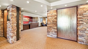 A hotel lobby with stone pillars, a reception desk, and a carpeted floor.