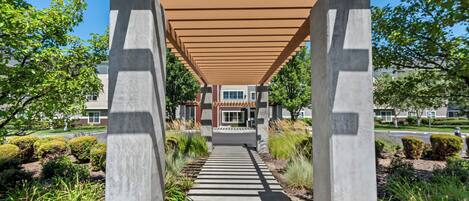 A pathway leading to a building with a covered walkway supported by concrete pillars.
