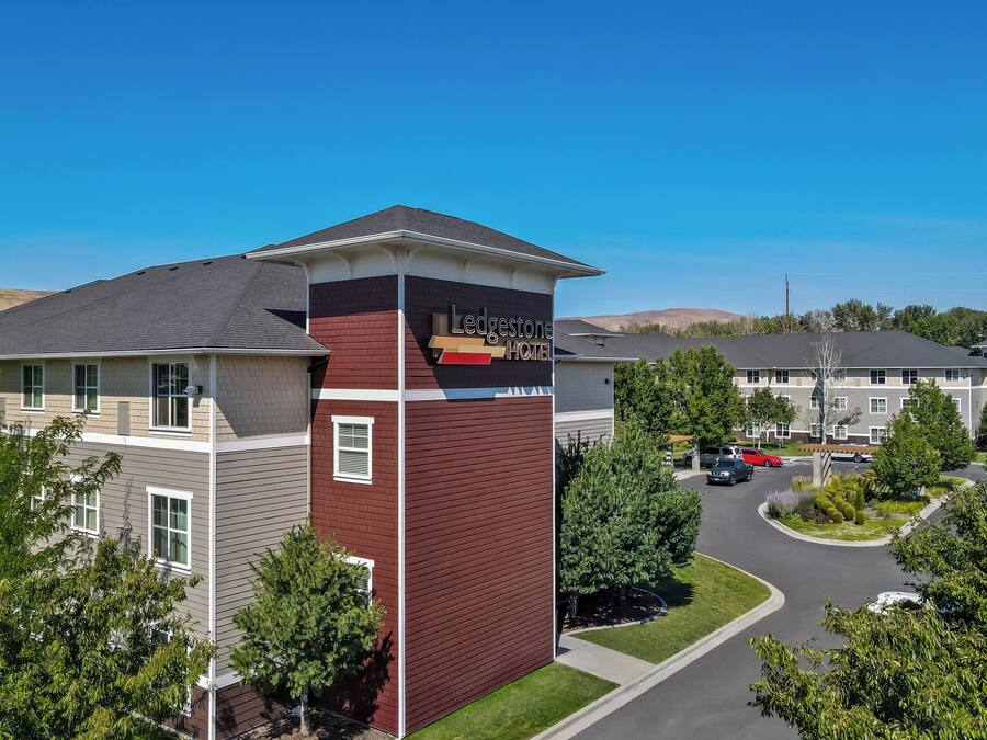 A hotel with a prominent red and beige facade, a parking area, and surrounding greenery.