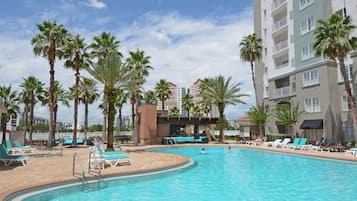 Relax by the resort pool surrounded by palm trees and lounge chairs.