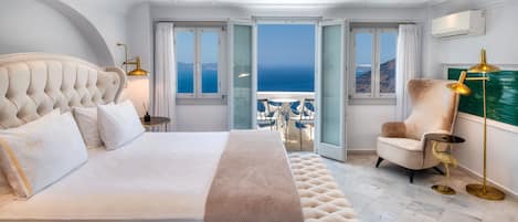 A bedroom with a large bed, a view of the sea, and a balcony with chairs.