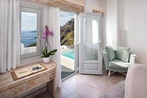 A balcony with a view of the sea and mountains, a seating area with a cushioned chair, and a small table with a plant and a photo album.