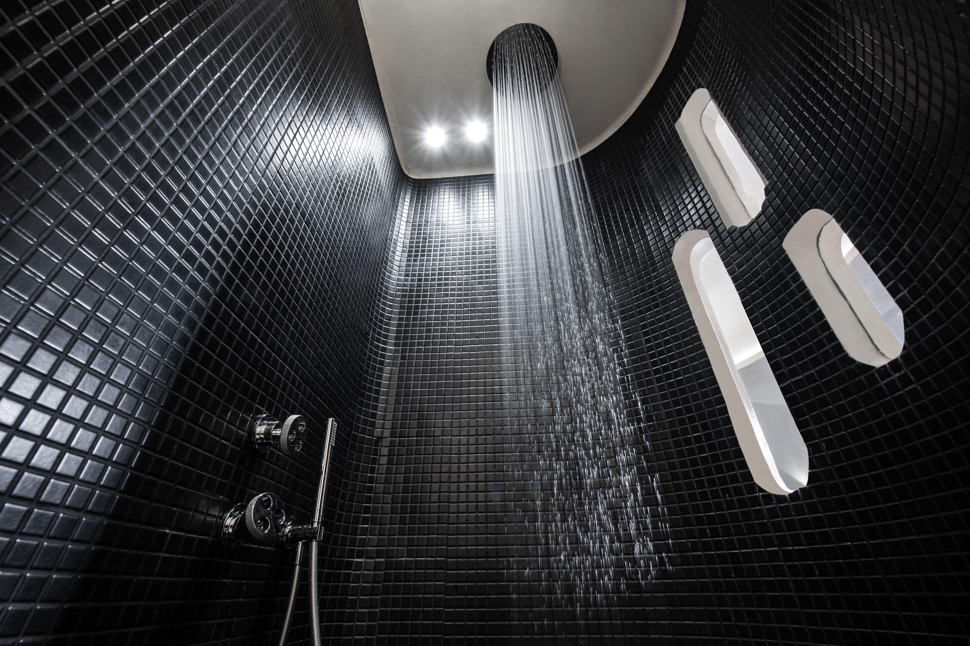 Un baño moderno con piso de baldosas negras, un cabezal de ducha y dos objetos rectangulares blancos en la pared.