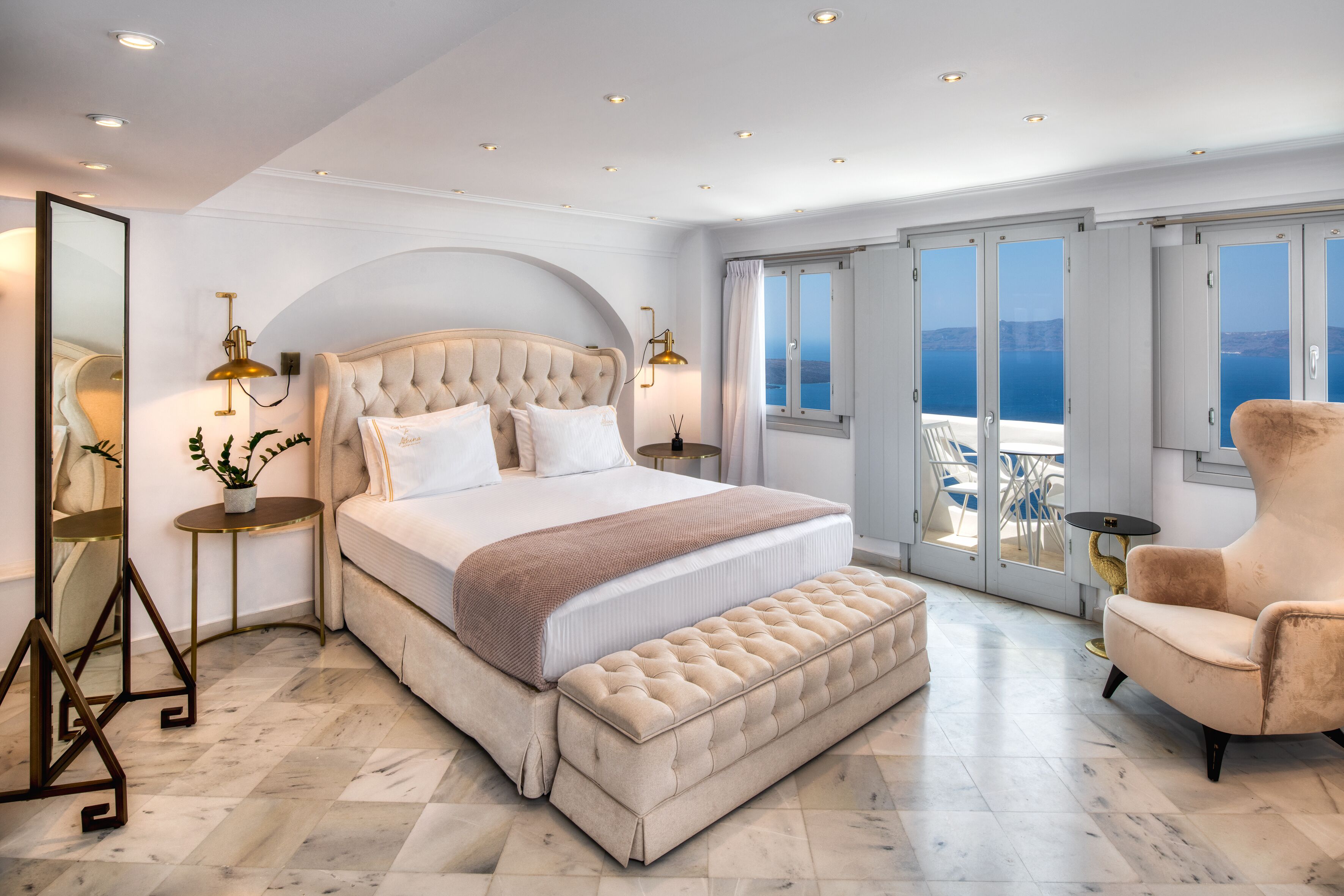 A spacious bedroom with a large bed, a sitting area, and a balcony with a view of the sea.