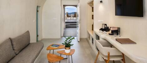 A modern interior with a sofa, a small dining area with stools, a table with a plant, and a TV mounted on the wall.