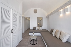 A modern, minimalist room with a sofa, a small round table with a bottle and glasses, and a large mirror above the sofa.
