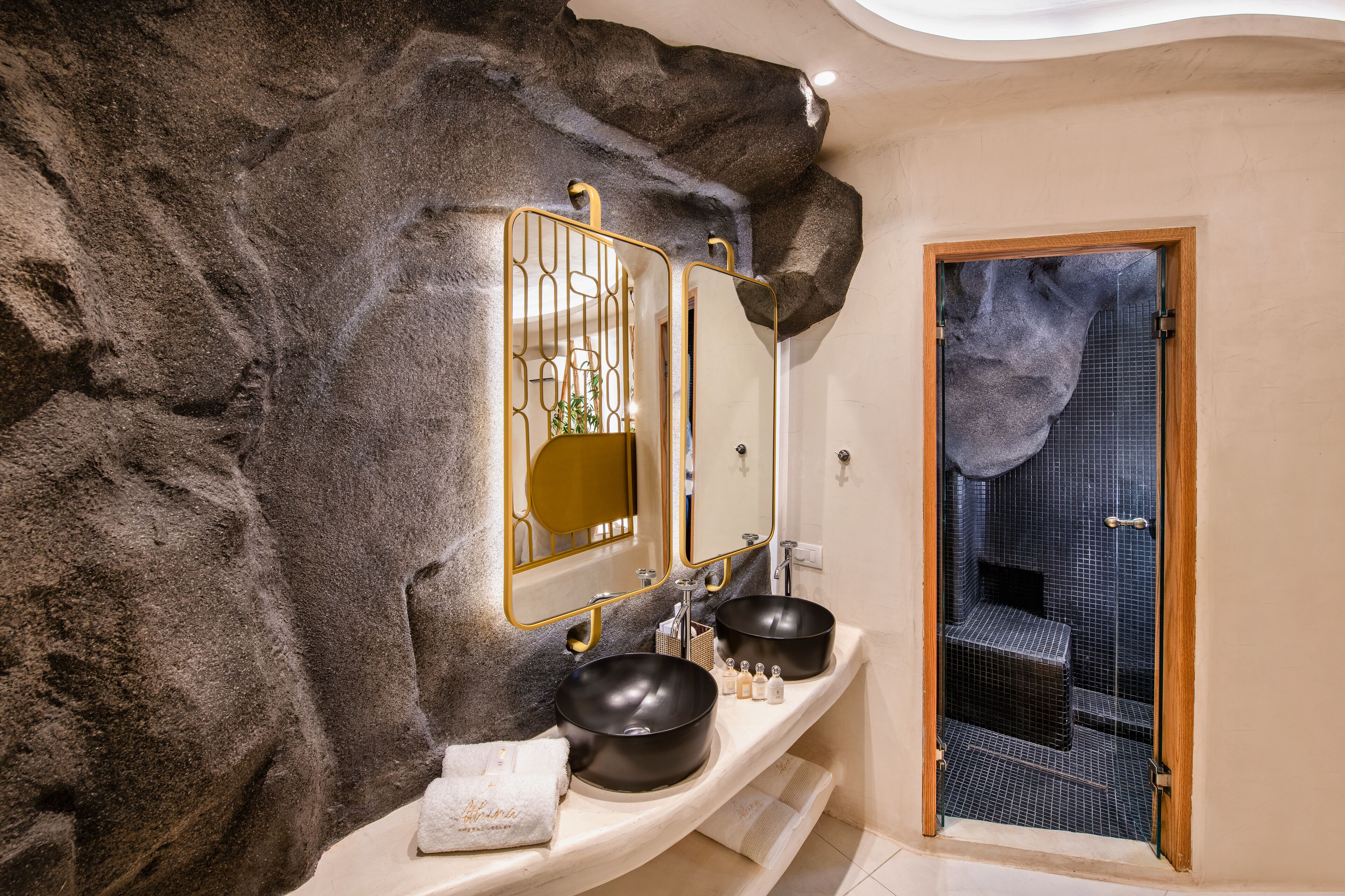 A bathroom with a large rock wall, two sinks, and a mirror.