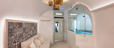 A hallway with a white sofa, wicker basket, and a glass-enclosed shower area.