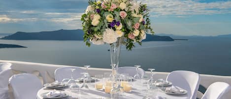 A table set for a meal with a floral centerpiece, overlooking a body of water and distant land.