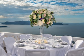A table set for a meal with a floral centerpiece, overlooking a body of water and distant land.