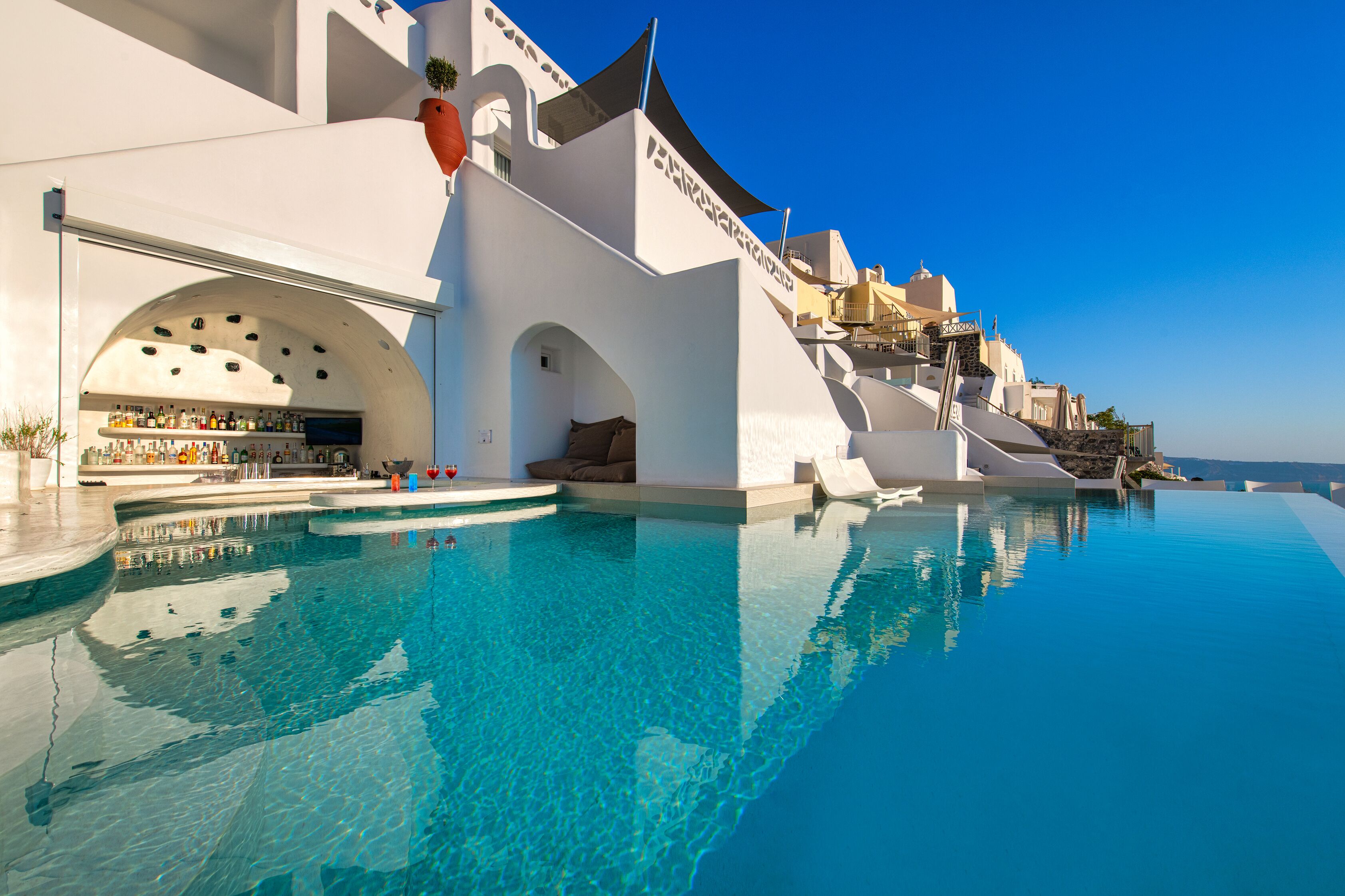 A modern hotel with a infinity pool, white architecture, and a bar area.