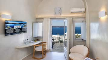 A room with a TV displaying a menu, a wooden chair, a small table, and a view of the sea through an open door.