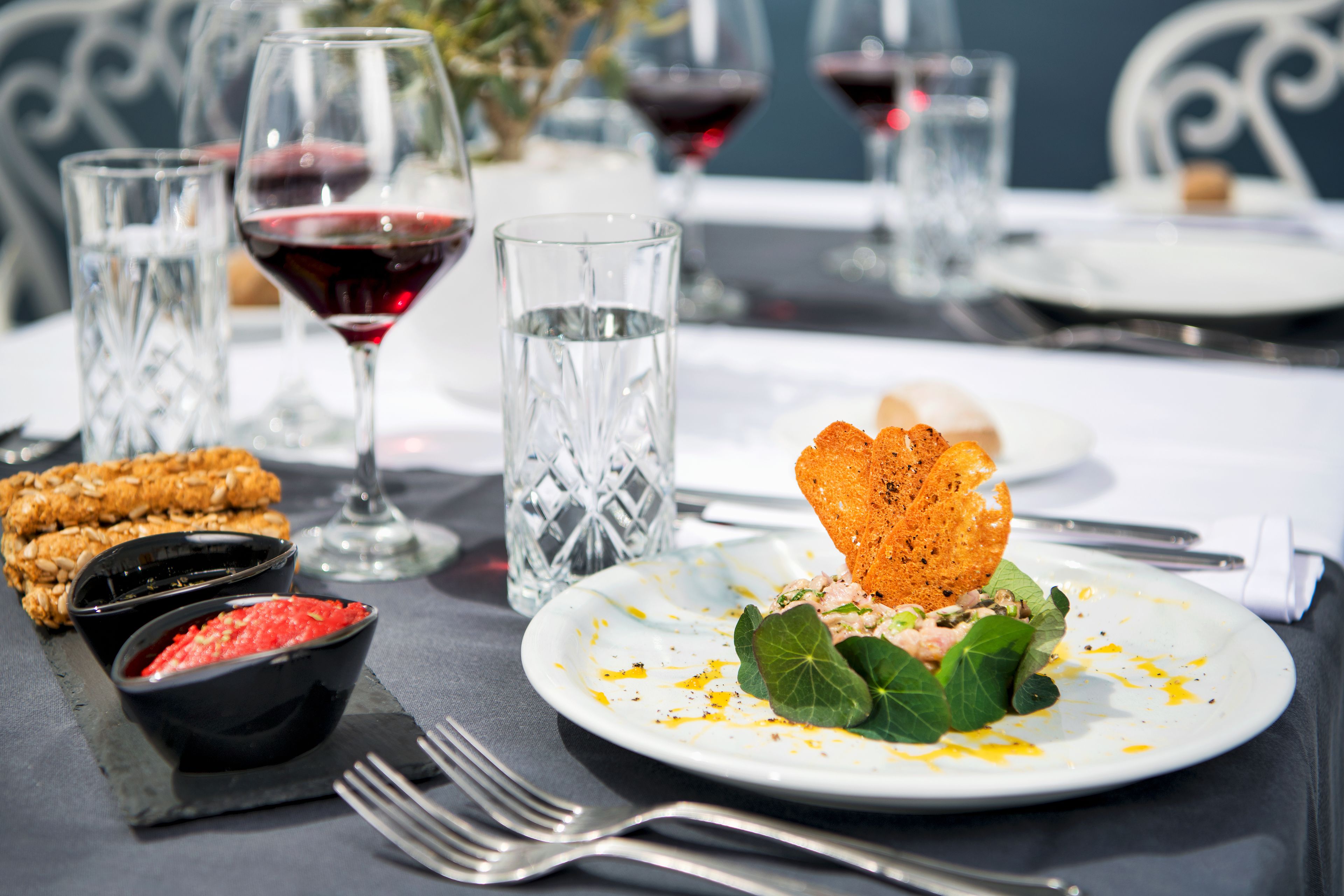 A dining table with a plate of food, two glasses of red wine, and a glass of water.