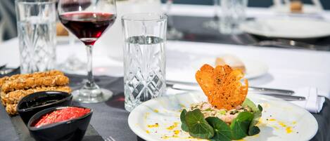 A dining table with a plate of food, two glasses of red wine, and a glass of water.