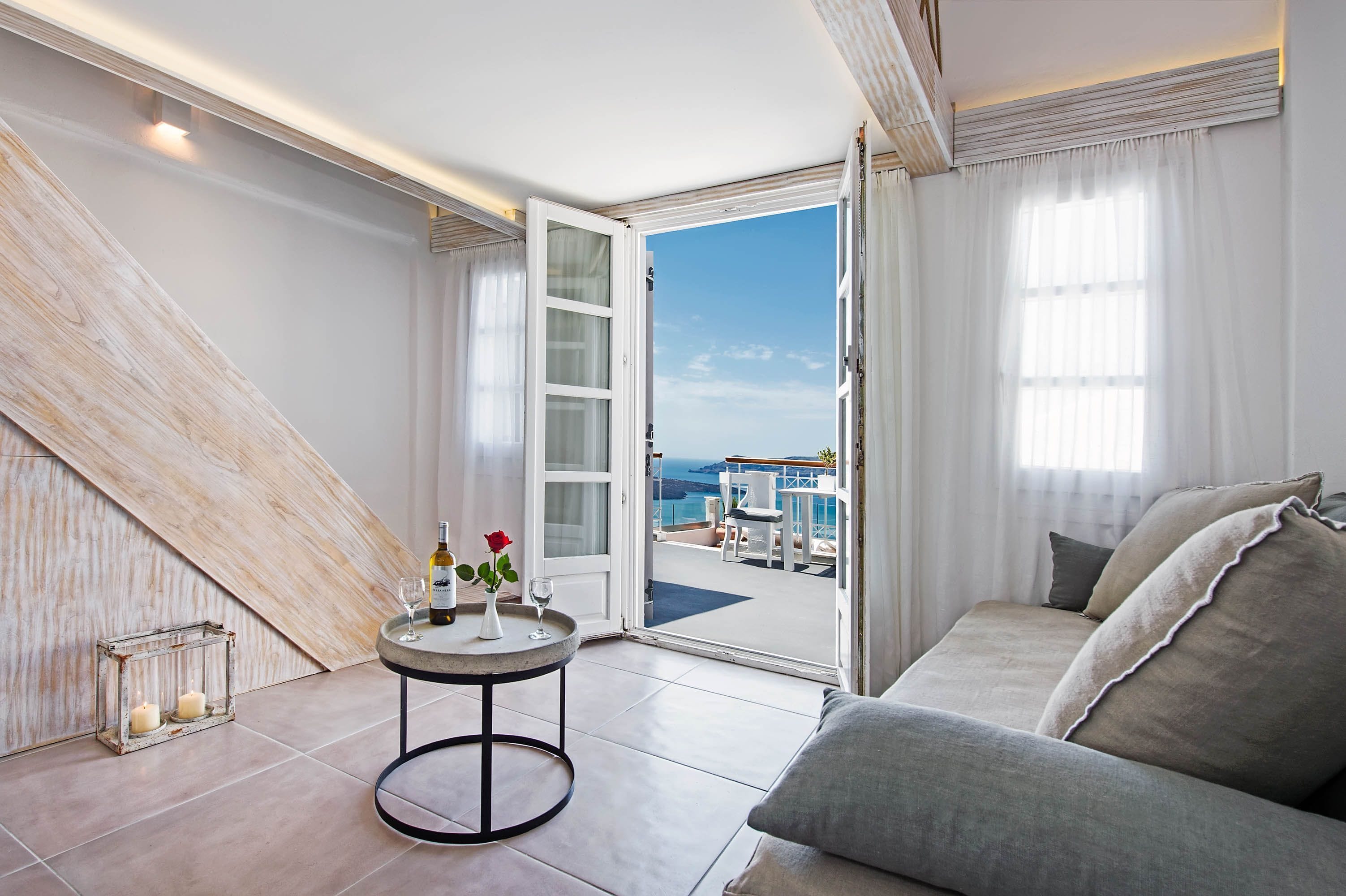 A modern room with a large window, a sofa, a small round table with candles, and a view of the sea.
