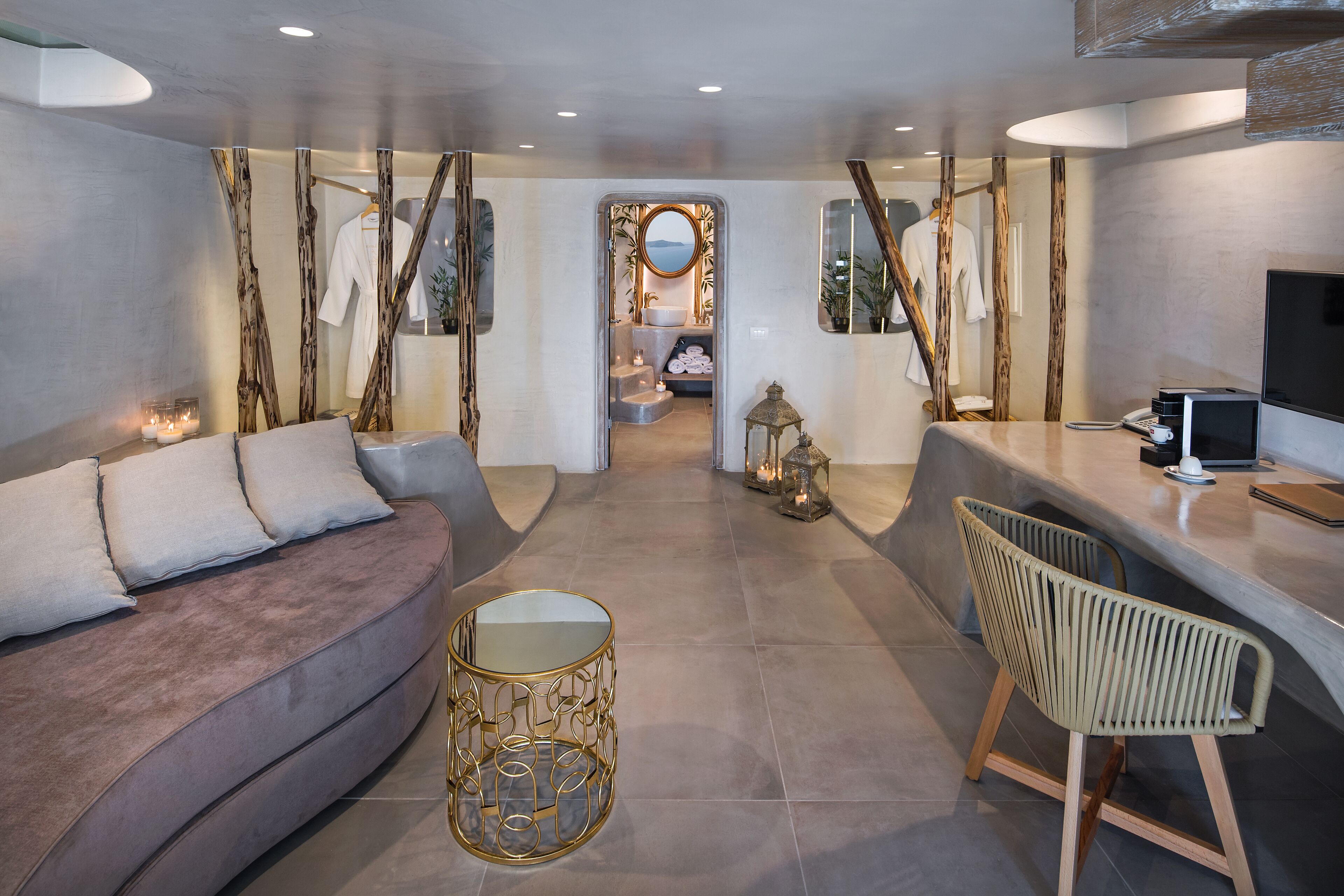 A modern hotel room with a sofa, a round table, a chair, and a view of the bathroom.