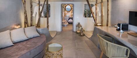 A modern hotel room with a sofa, a round table, a chair, and a view of the bathroom.