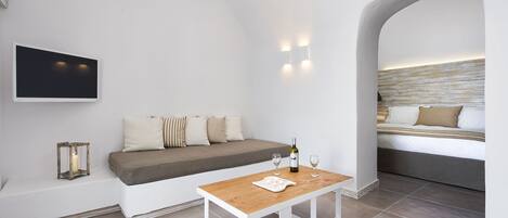 Een moderne, minimalistische kamer met een houten tafel, een witte bank en een bed met hoofdeinde.