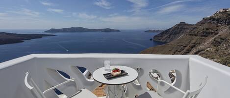 A balcony with white chairs and a small table with a dessert and a glass.