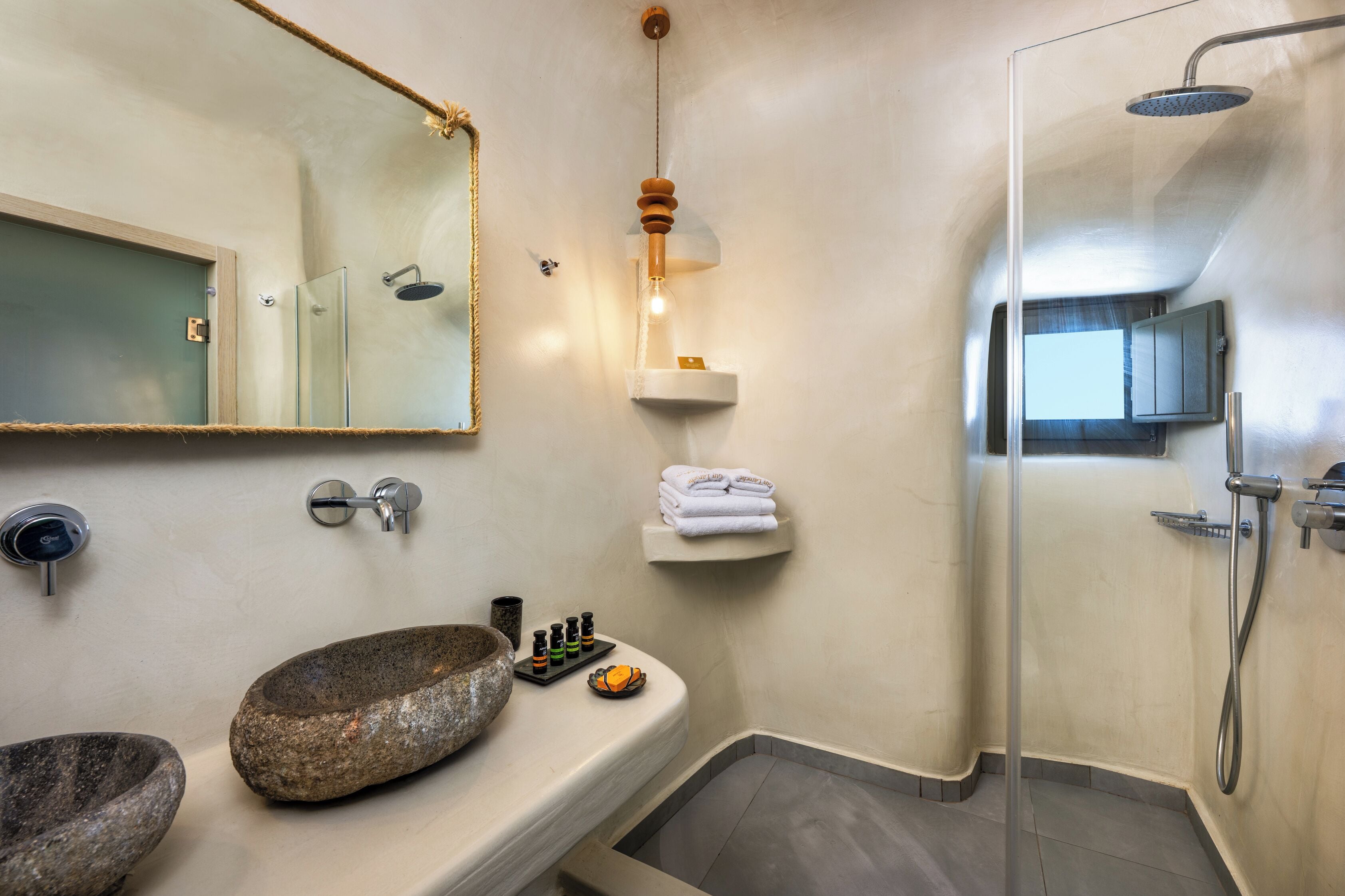 A bathroom with a stone sink, a mirror, a shower, and a shelf with towels.