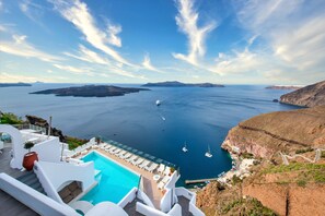 A resort with a pool, lounge chairs, and a view of the sea and islands.