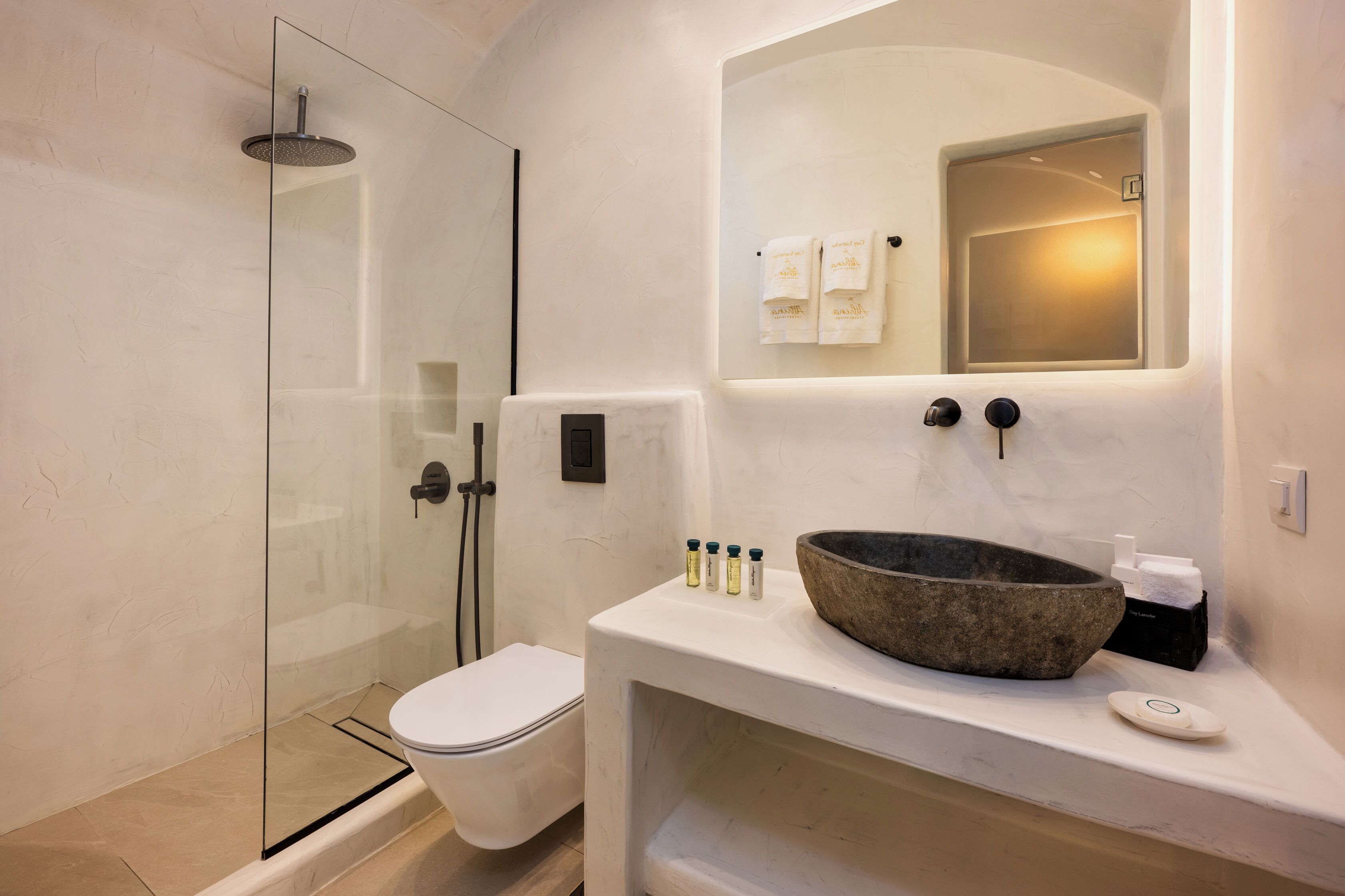 Un baño moderno con cabina de ducha de vidrio, inodoro blanco y un lavabo de piedra grande con espejo superior.