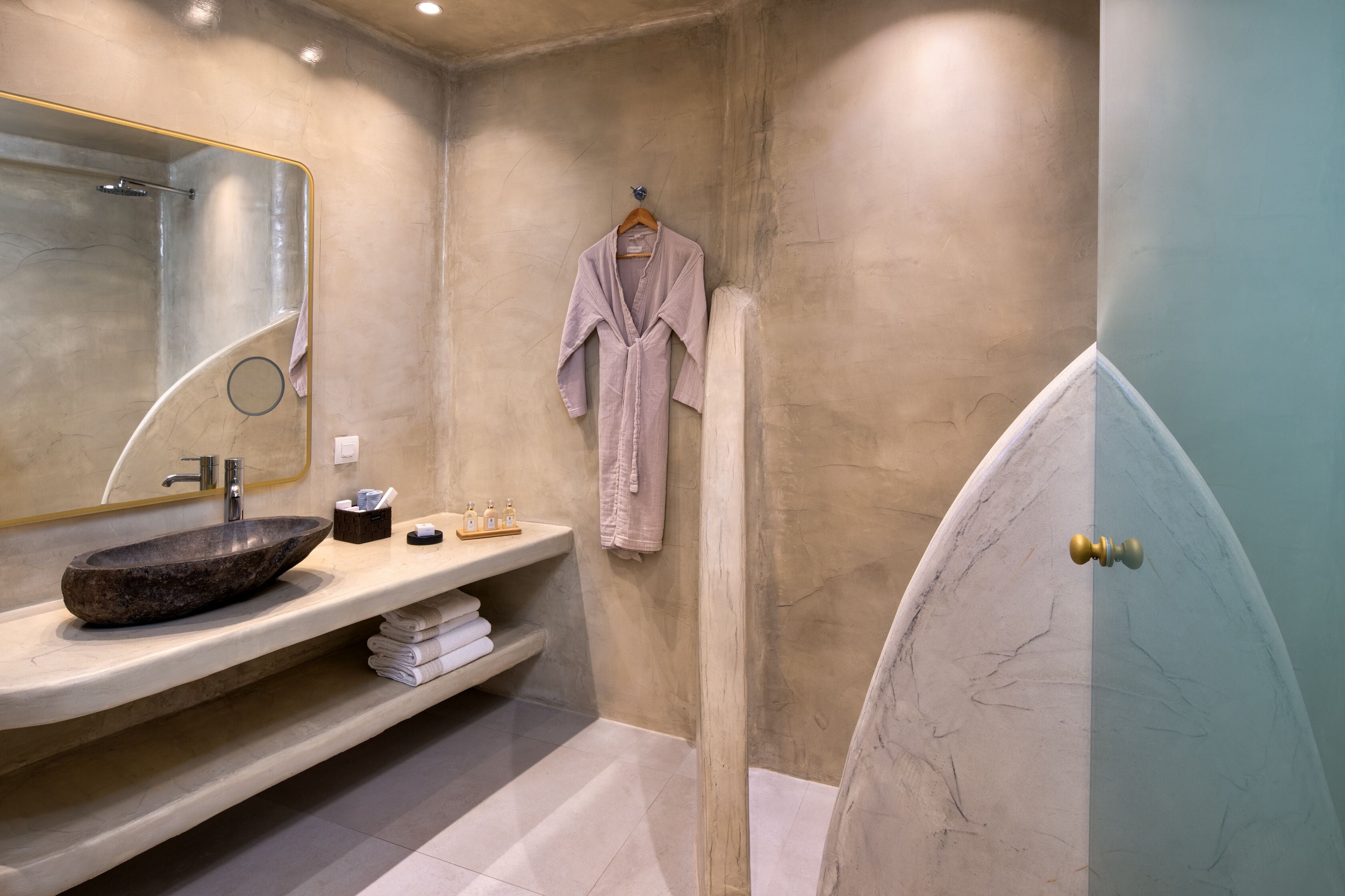 A bathroom with a marble sink, a robe hanging on a rack, and a shower area.