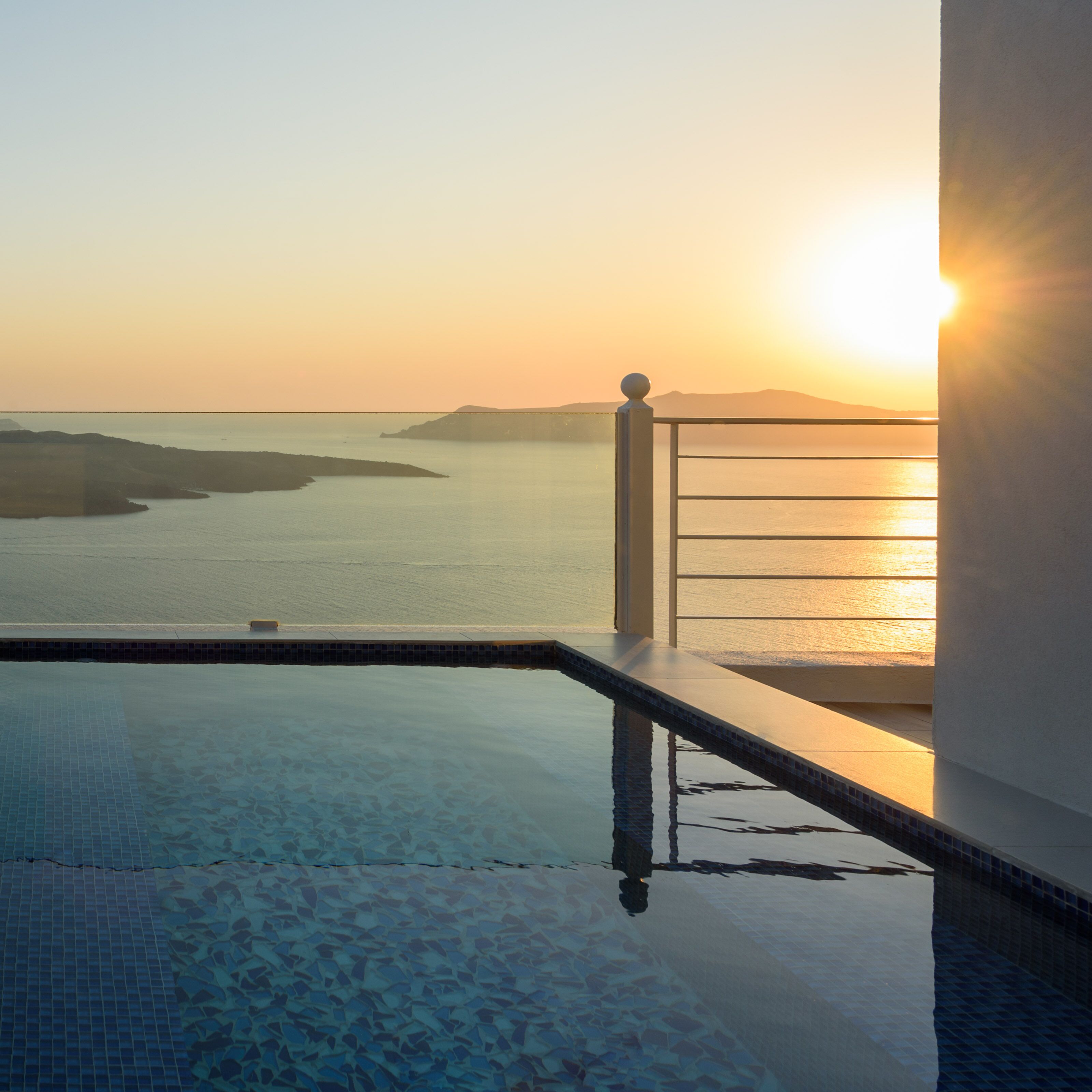 A swimming pool with a view of the sea and a sunset.