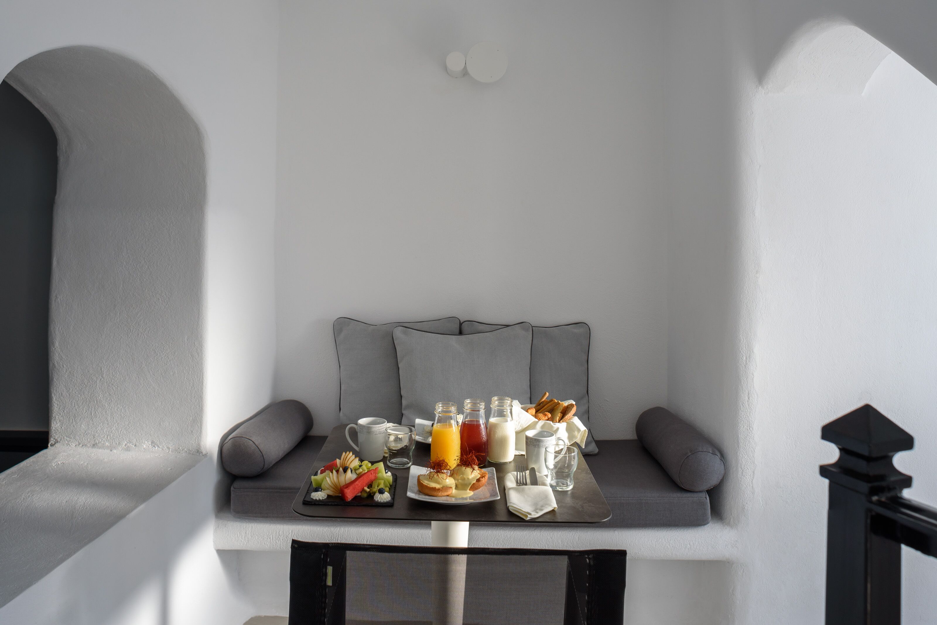 A breakfast setup with a tray of food, beverages, and a cup of coffee on a cushioned bench.