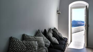Una sala de estar moderna con un sofá negro y cojines estampados, una pared blanca y vistas a las montañas desde una puerta abierta.