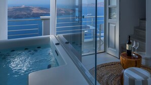 A modern balcony with a hot tub, a wine bottle, and glasses on a wooden side table. - Nefeles Luxury Suites (Santorini)