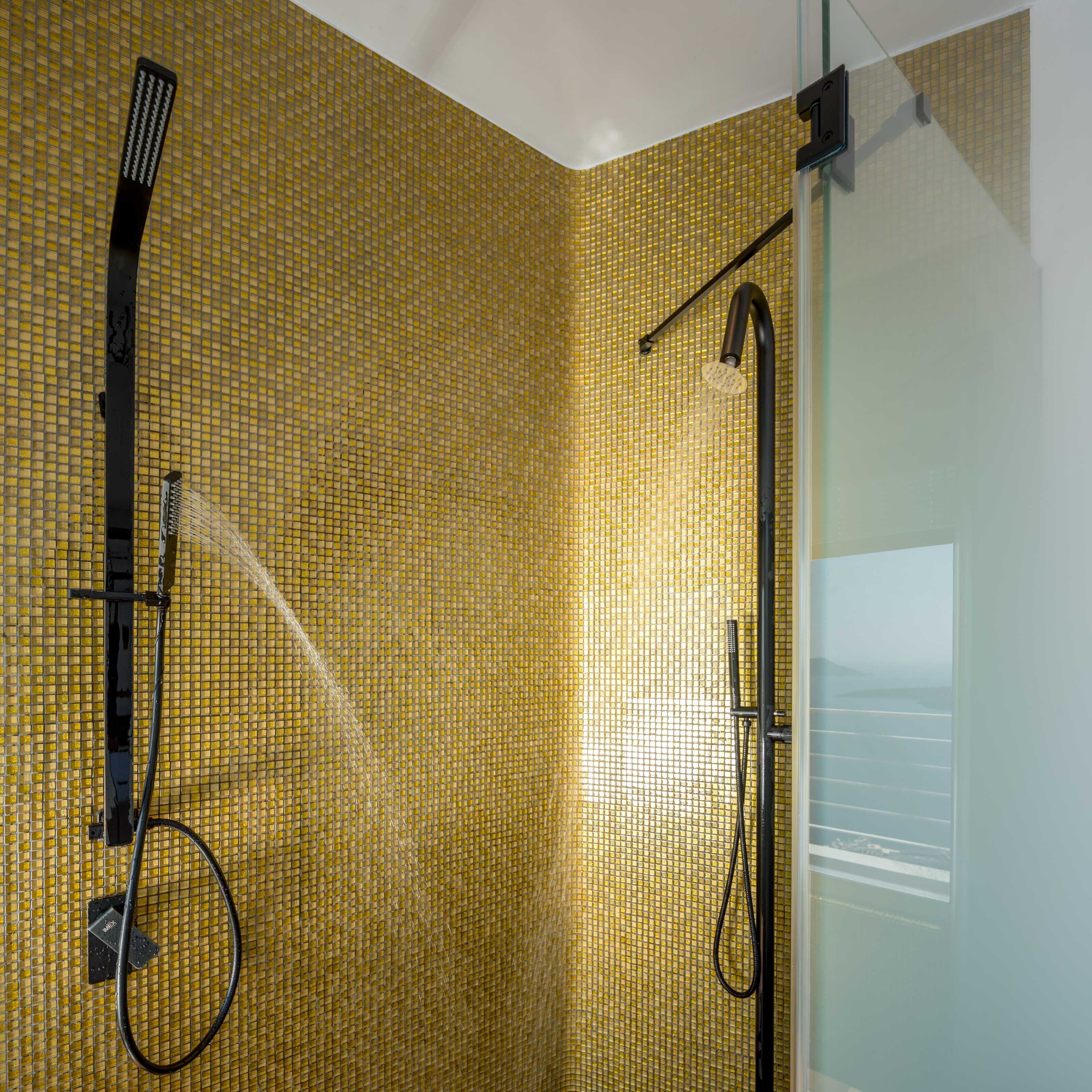 A shower with a golden mosaic wall, a handheld showerhead, and a wall-mounted faucet.