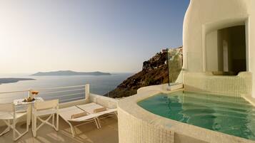 A sunlit terrace with a pool, white furniture, and a view of the sea and distant islands.