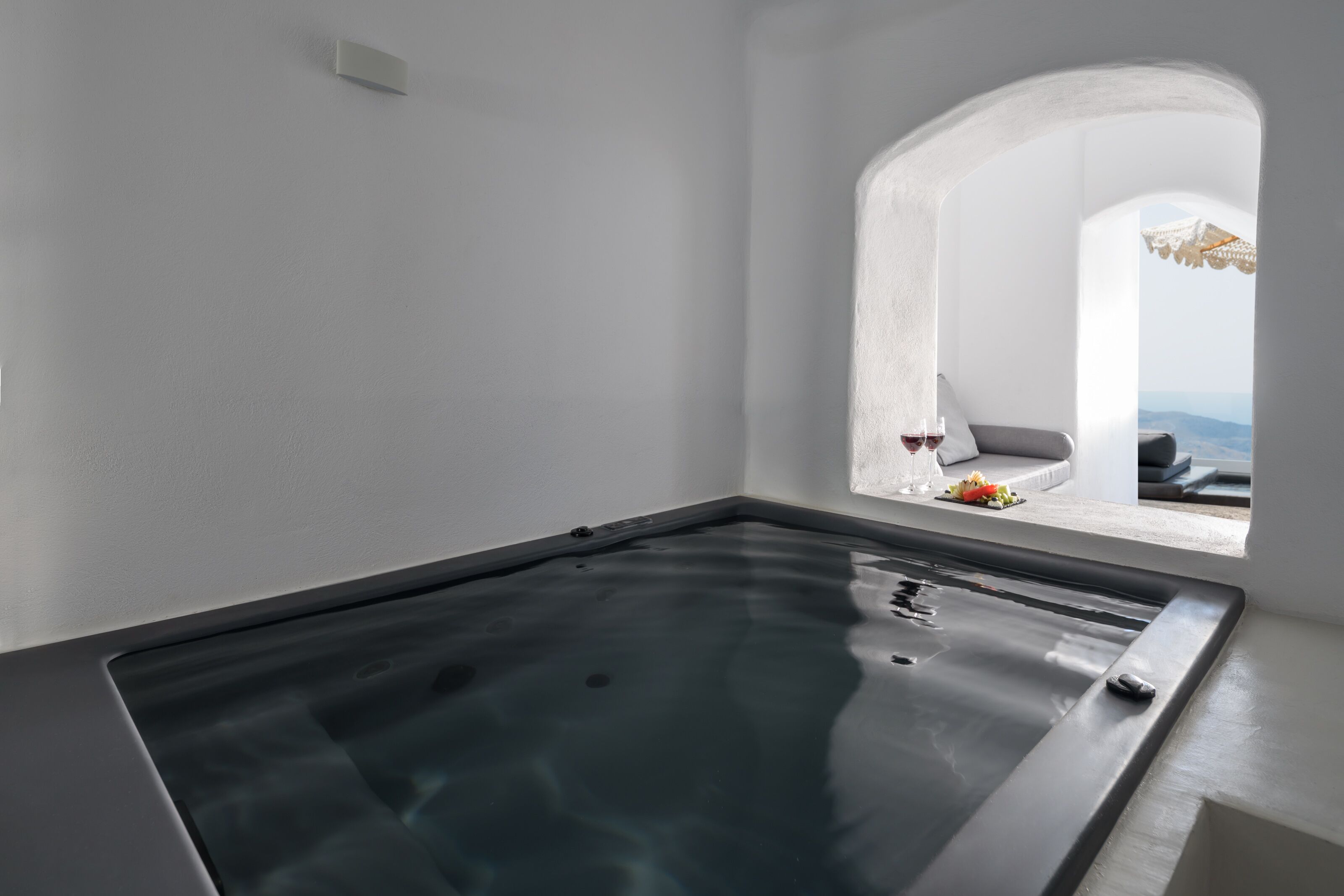 A spa area with a large hot tub, a view of the outdoors through an arched window, and a small seating area with a table and flowers.