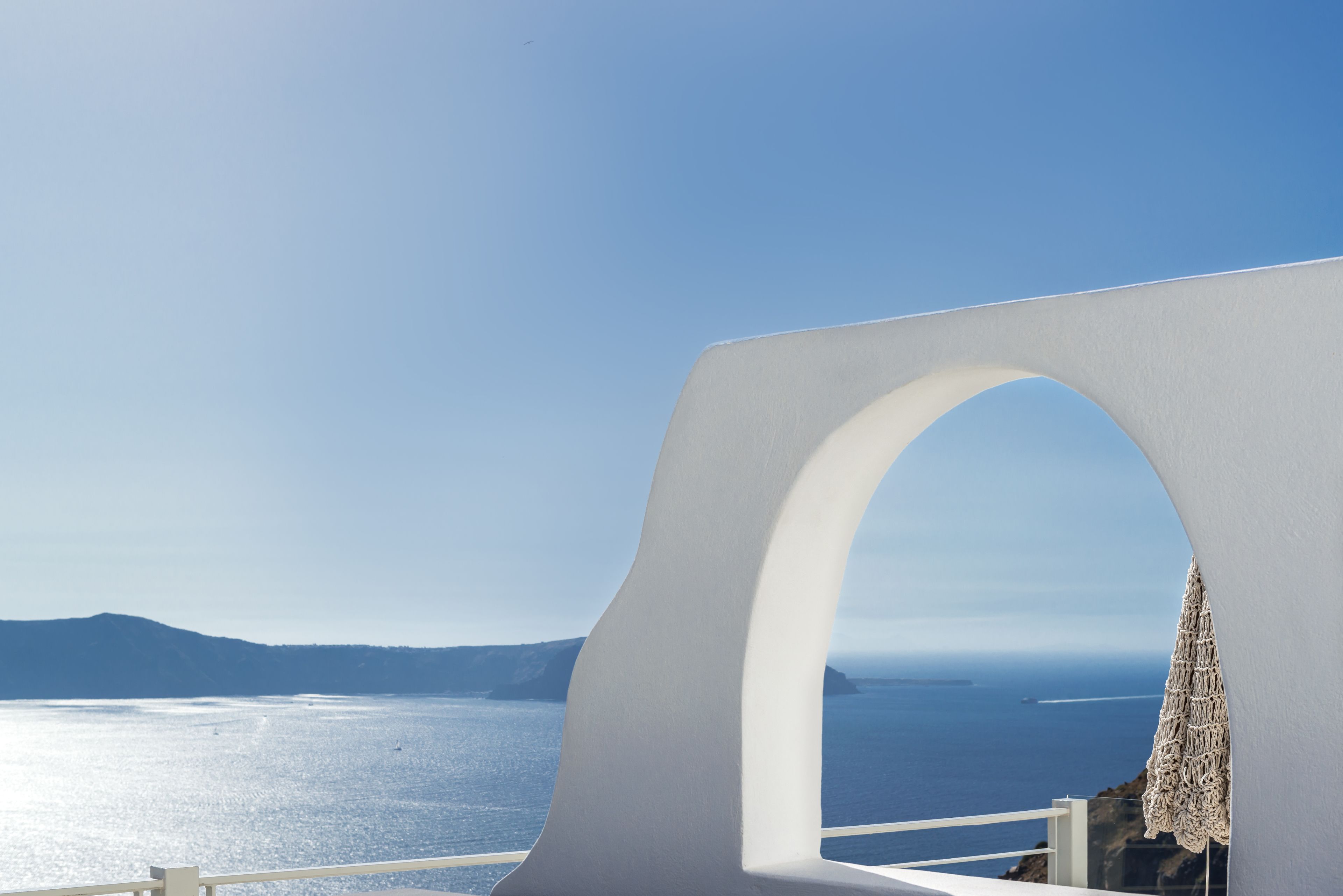 A white architectural structure with a view of the sea and distant mountains.