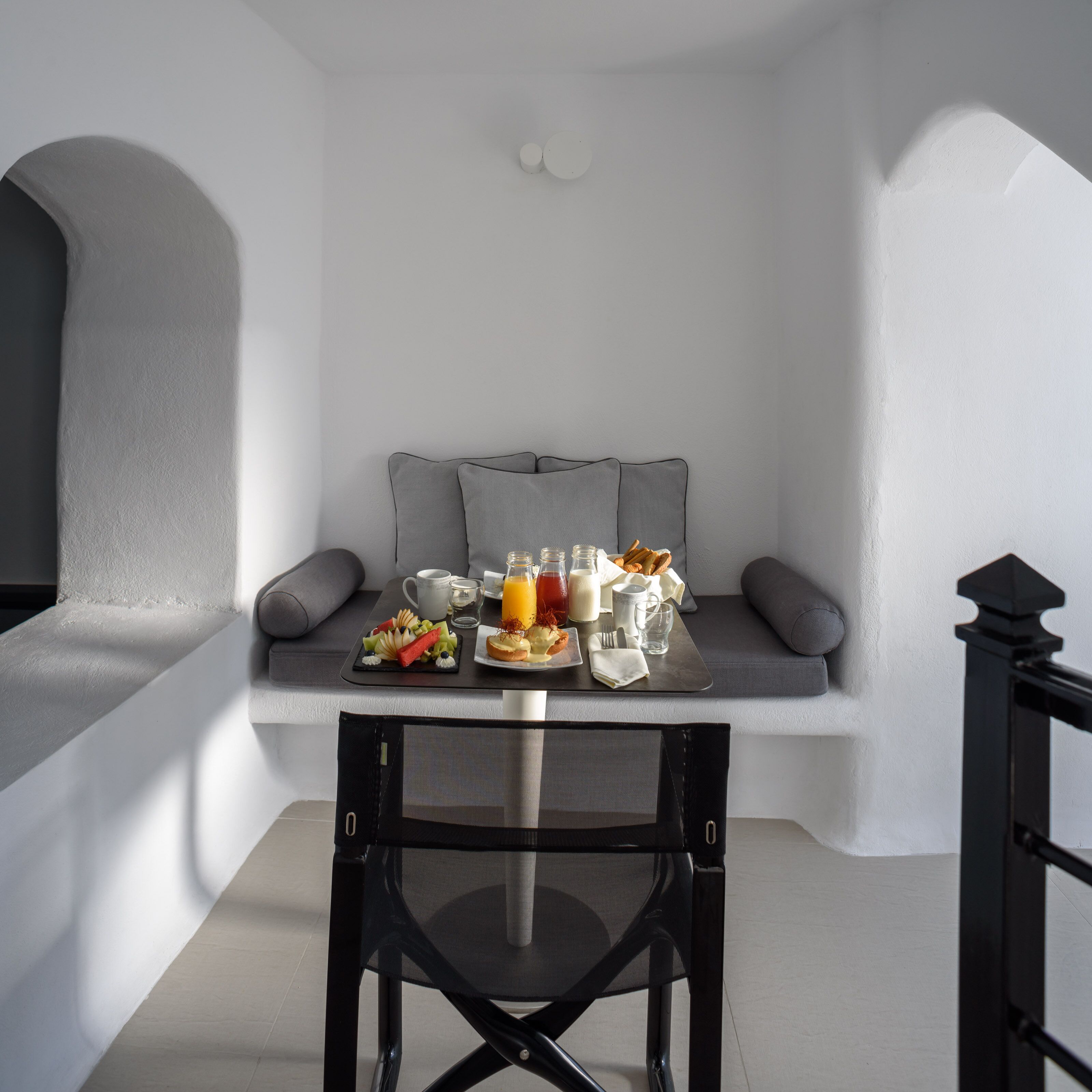 A breakfast setup with a table, seating, and a chair in a room with white walls and a window.