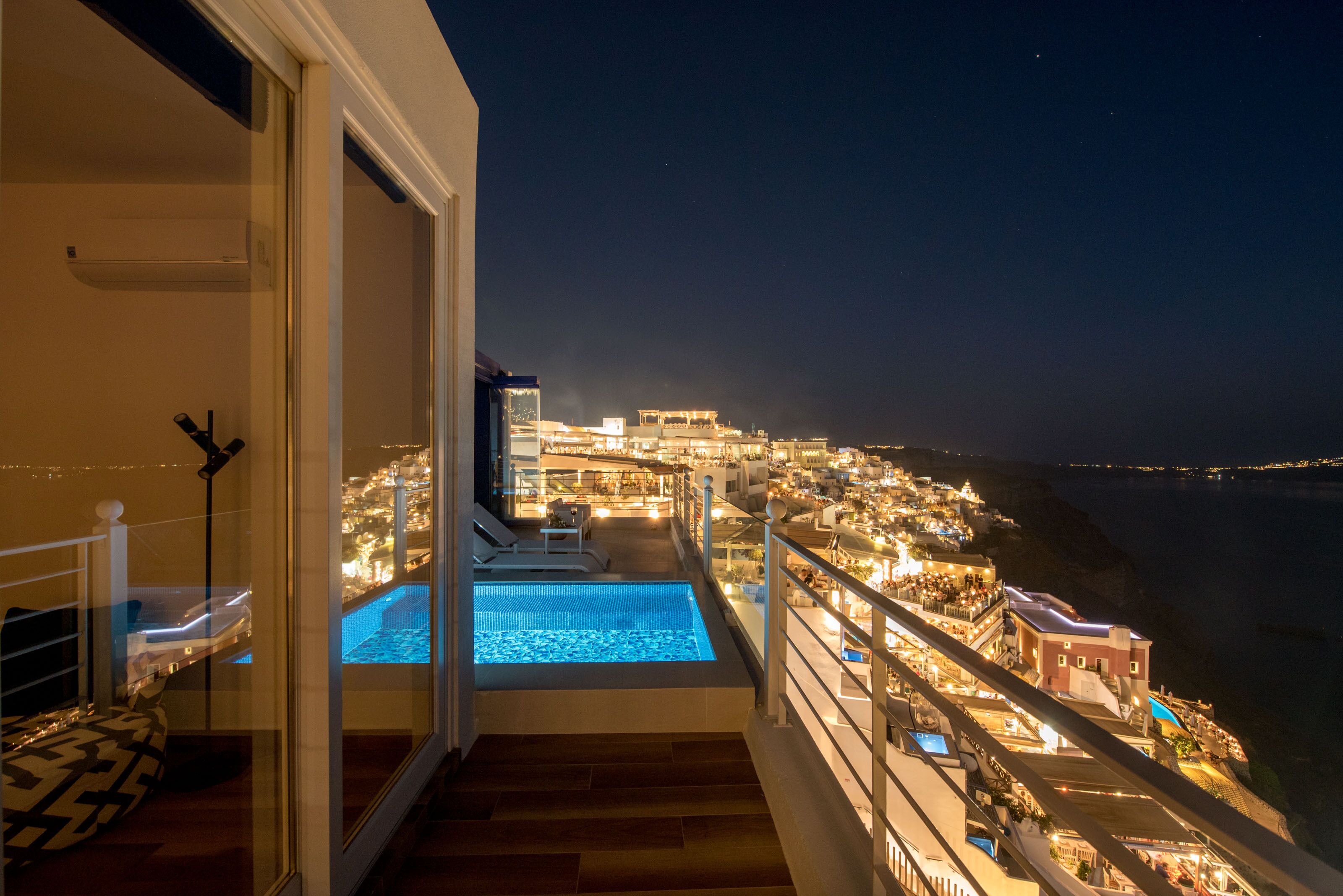 A balcony with a pool, overlooking a cityscape at night.