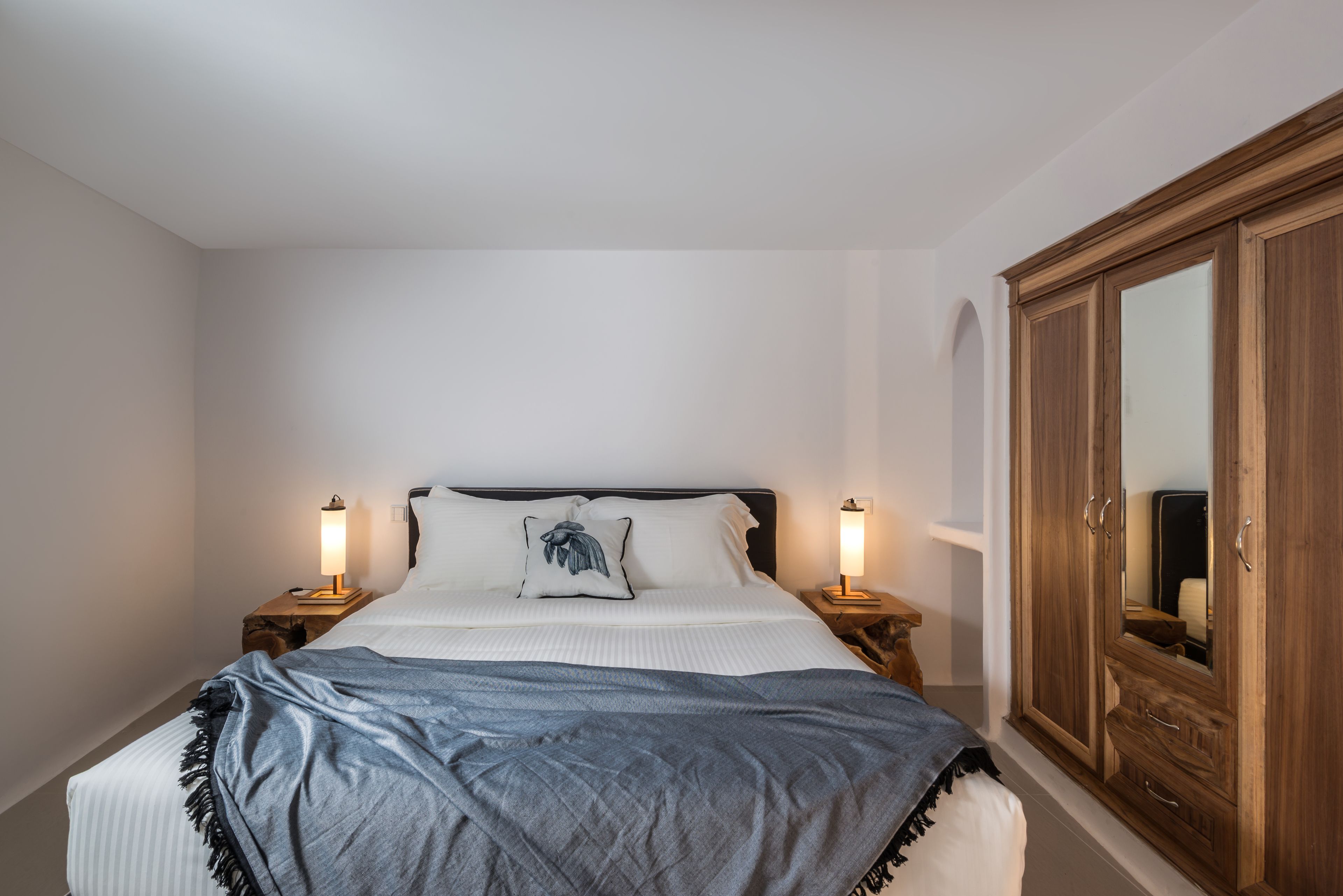 A bedroom with a bed, bedside lamps, a wardrobe, and a mirror.