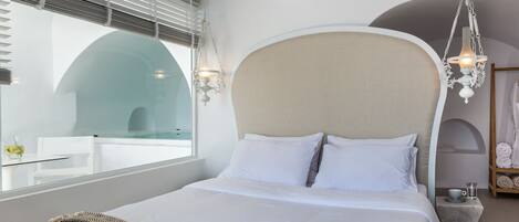 A modern bedroom with a large bed, white bedding, a patterned throw, a hanging light fixture, and a view of a glass-walled room.