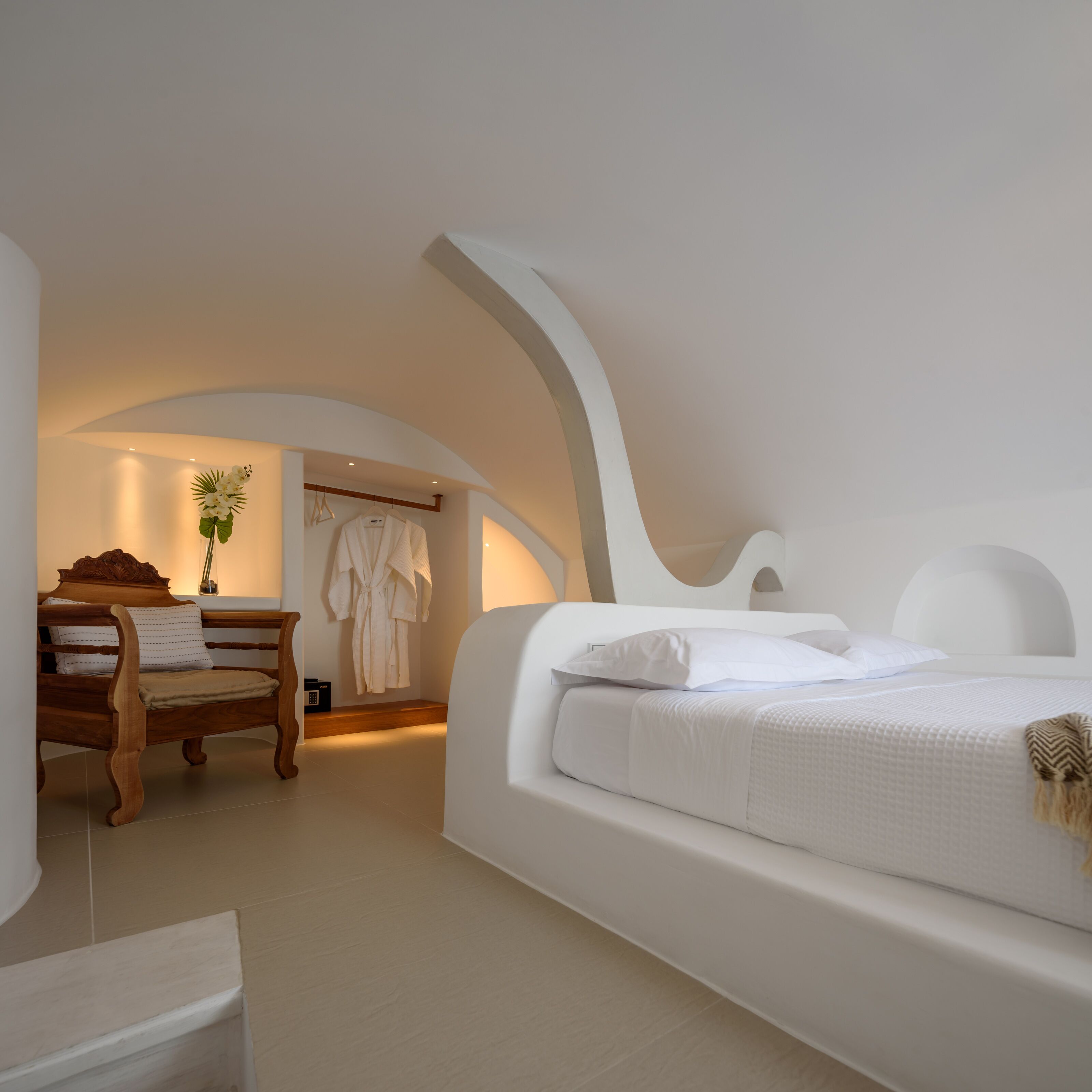 A bedroom with a curved ceiling, a wooden bench, a robe, and a bedside table.