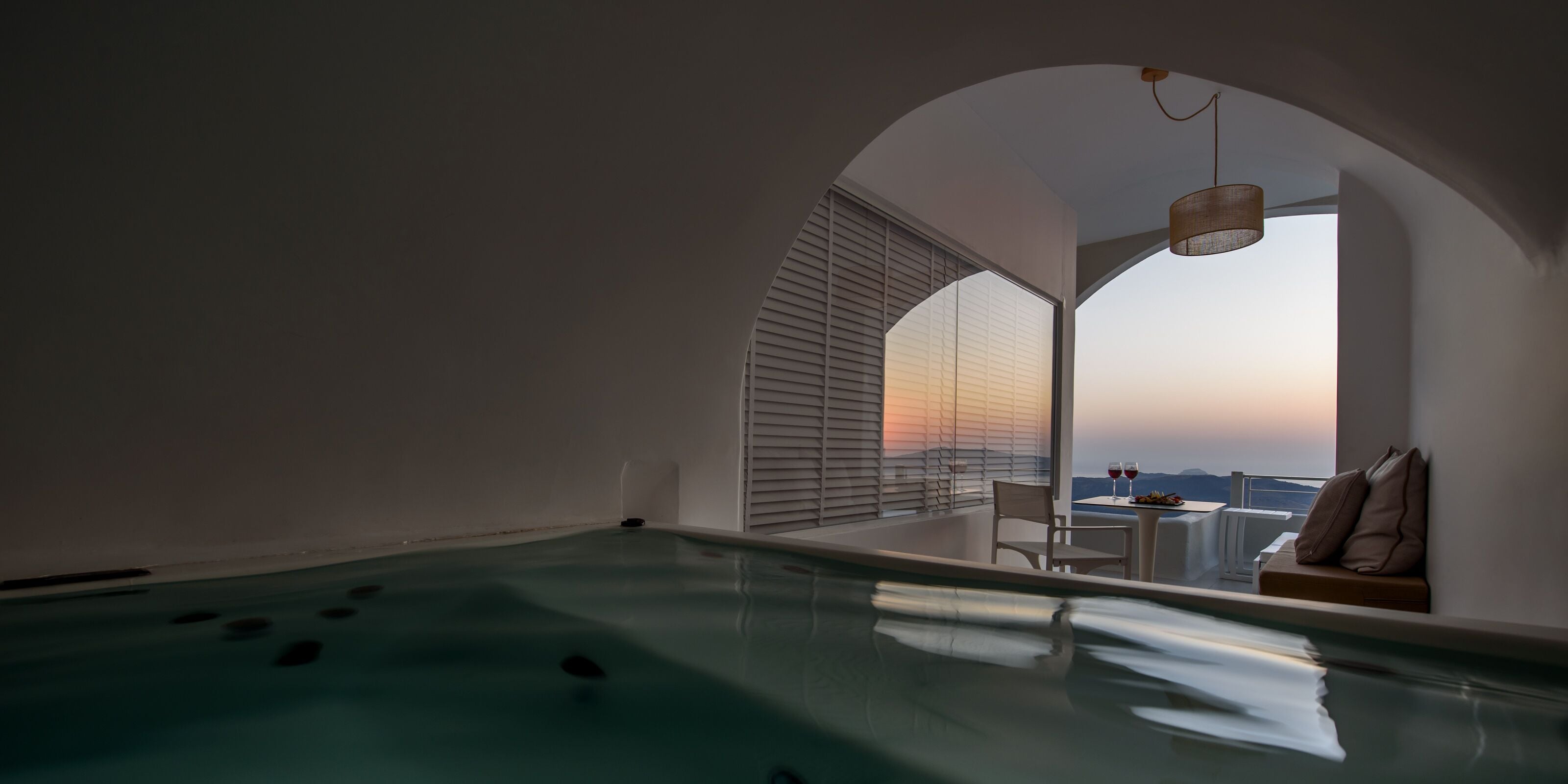 A modern indoor pool with a view of the sunset through arched windows.