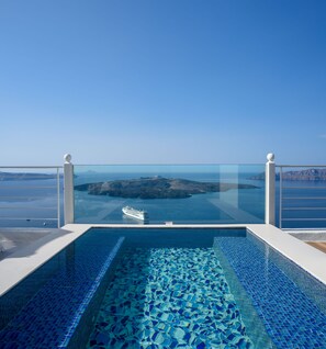 A clear view of a swimming pool with a glass barrier, a cruise ship in the distance, and a mountainous landscape. - Nefeles Luxury Suites (Santorini)