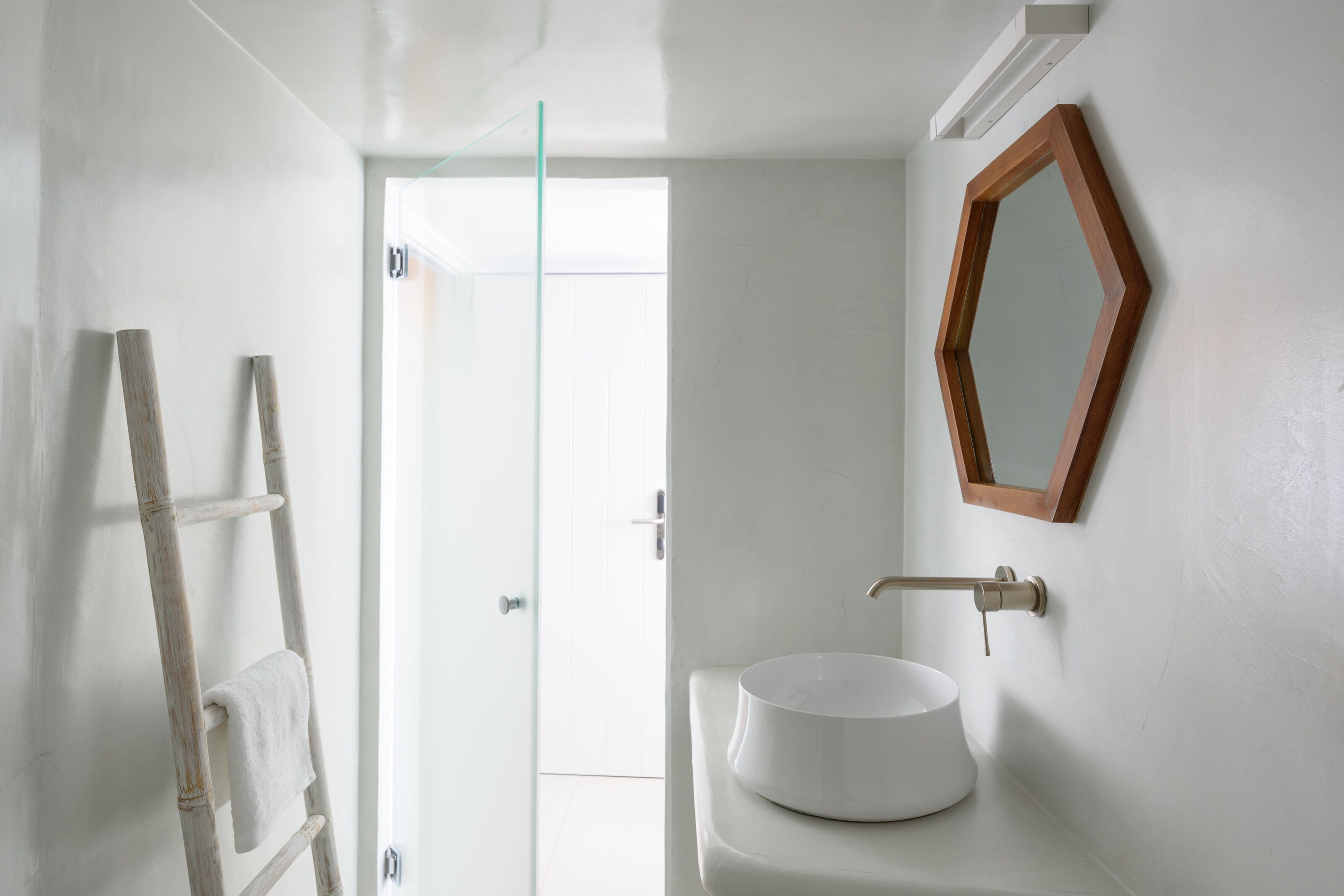 A bathroom with a white sink, a wooden ladder, and a wooden-framed mirror.