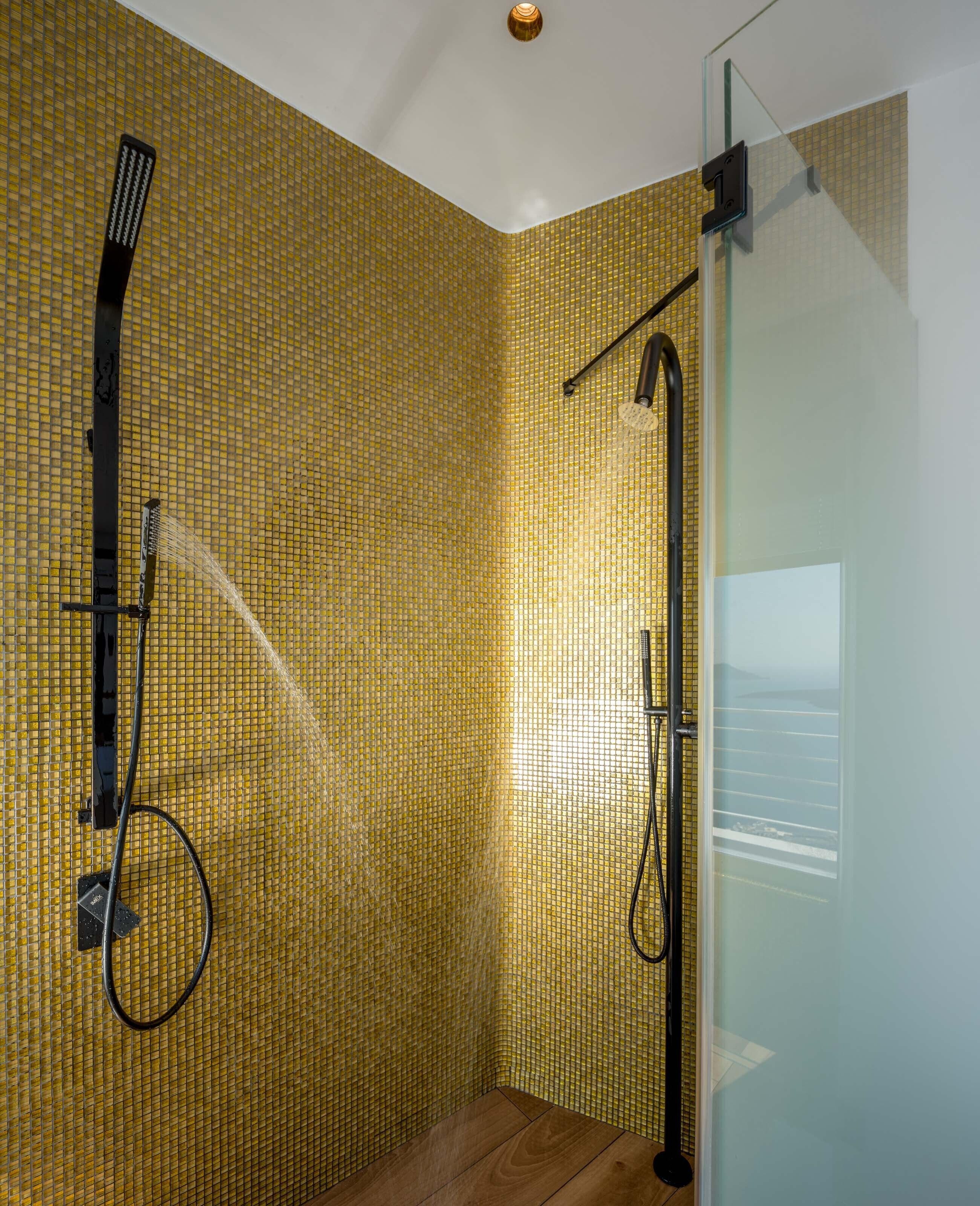 Ducha con puerta de vidrio y pared revestida de azulejos amarillos.