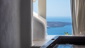 A room with a view of the sea, a bathtub, and a window with curtains. - Nefeles Luxury Suites (Santorini)