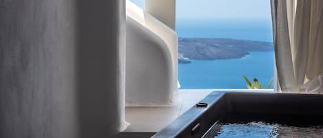 A room with a view of the sea, a bathtub, and a window with curtains.