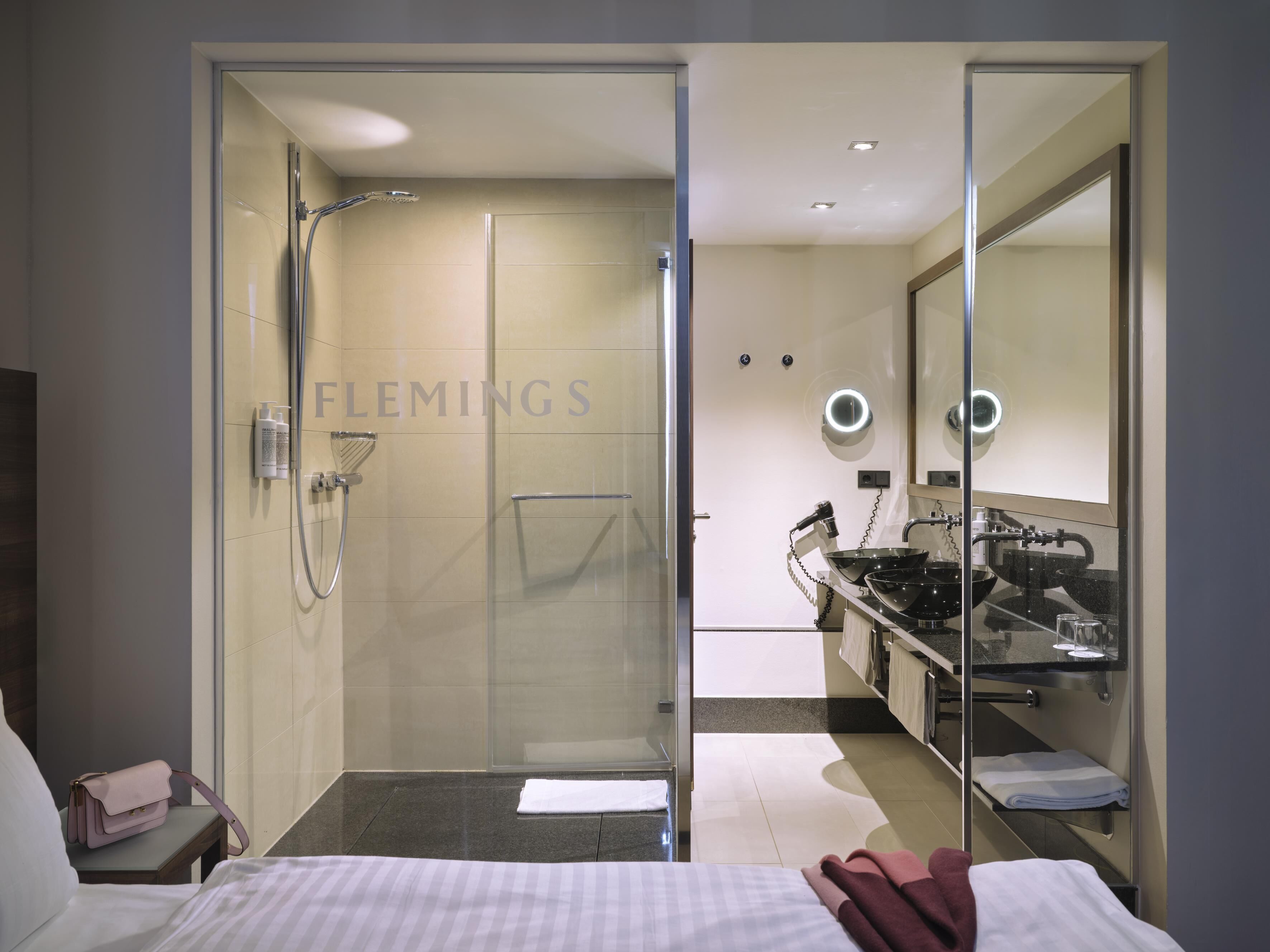 A modern hotel bathroom with a glass-enclosed shower, a vanity with a black sink, and a large mirror.